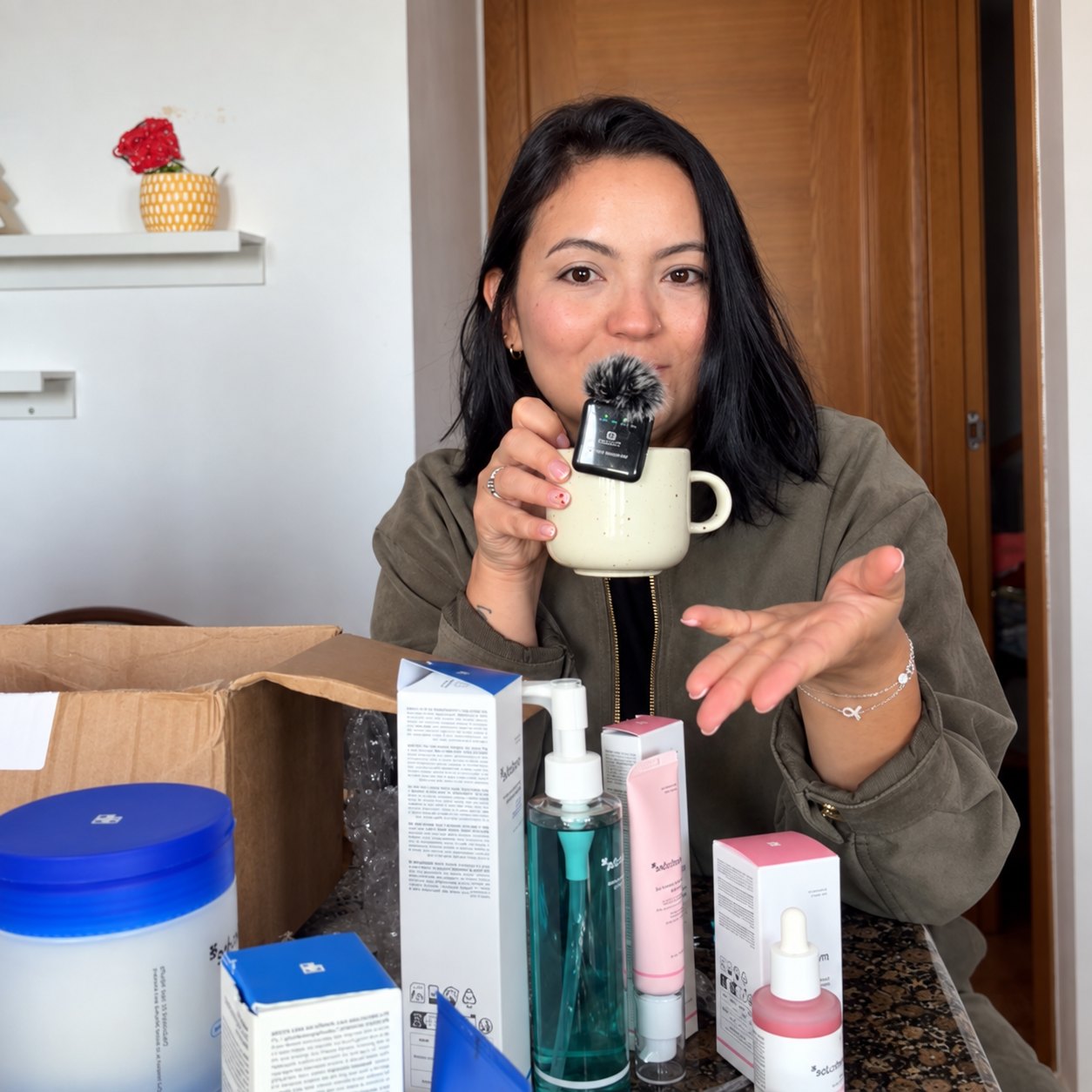 Génesis en casa presentando productos de cuidado de la piel con un micrófono en la mano